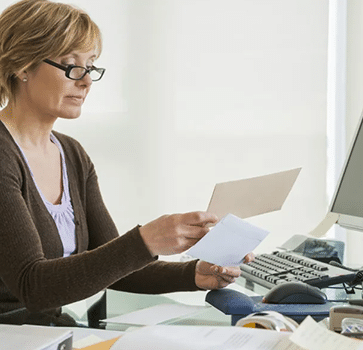 Woman in office reviewing document at desk with laptop and dental equipment visible.