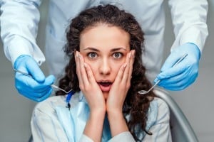 Surprised woman in dental chair with dentist's gloved hands on either side of her face.