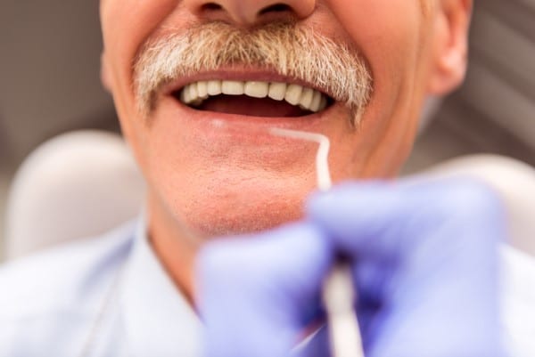 Dentist examining patient's teeth during dental checkup with gloved hands in clinical setting.