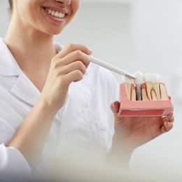 Smiling dental professional holding dental implant model in clinical office setting.