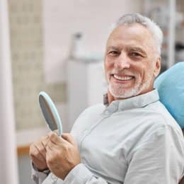 Smiling senior man holding dental mirror in dental office chair at Danville Family Dental.
