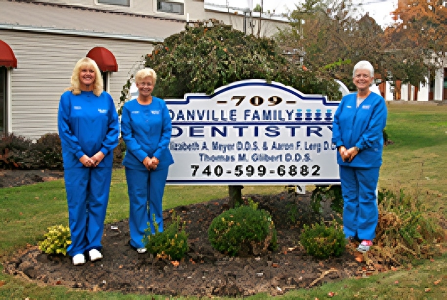 Four dental staff members in blue scrubs holding Danville Family Dentistry sign outside office building.