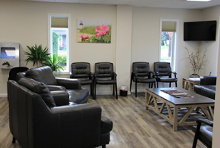 Modern dental waiting room with black leather seating, plants, and wall-mounted television.