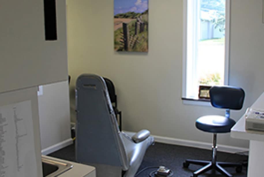 Dental office treatment room with chair, overhead light, and sterilization equipment visible.